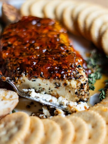 Cream cheese with spicy hot pepper jelly and crackers on a platter.