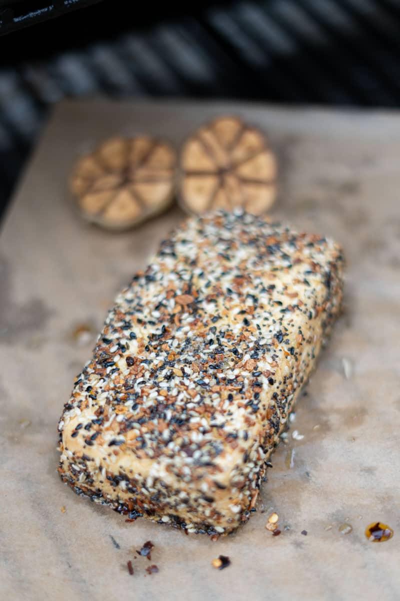 A seasoned cream cheese block sitting on a smoker grate, wreathed in light smoke