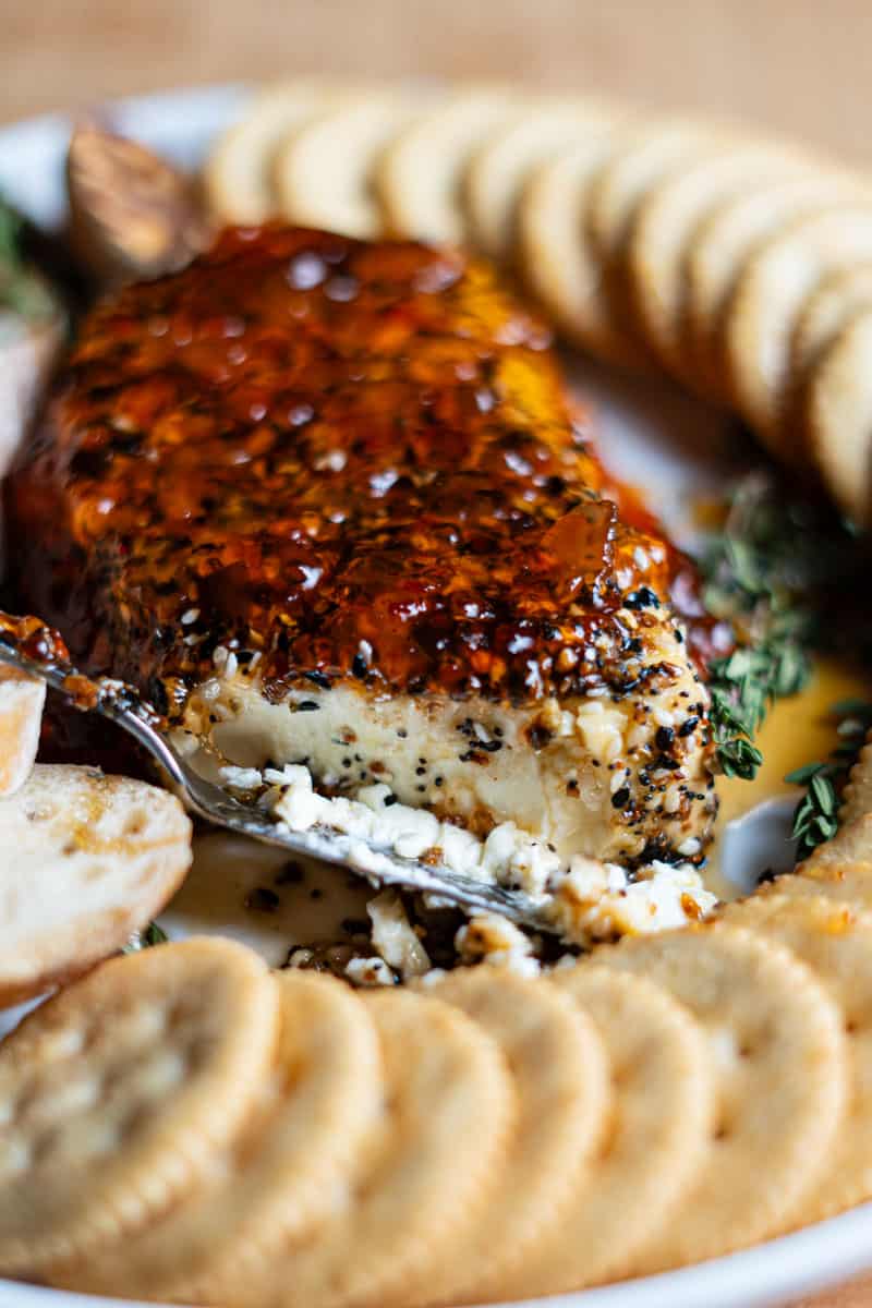 A block of smoked cream cheese topped with red hot pepper jelly and everything bagel seasoning, served on a cutting board with crackers