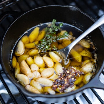 smoked garlic cooking in a cast iron pot on a smoker with fresh thyme and red peper flakes