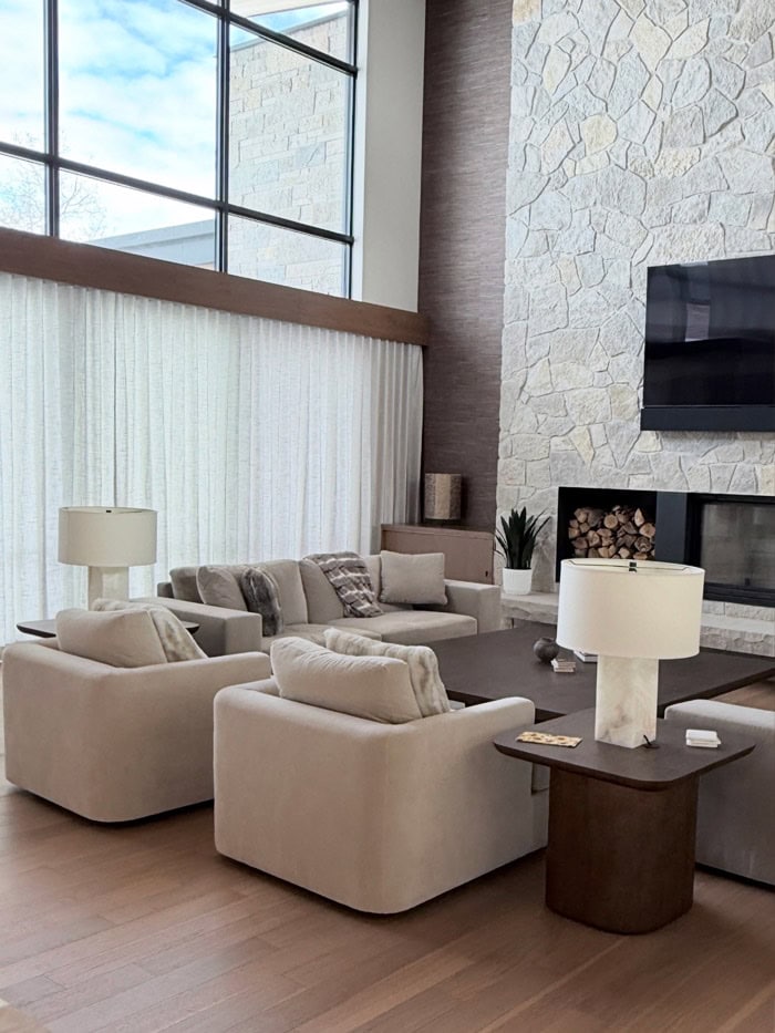 Modern living room with large windows and cozy beige sofas in a contemporary home. Bright, airy space with natural light, stylish decor, and a stone fireplace. Perfect for relaxing and entertaining.