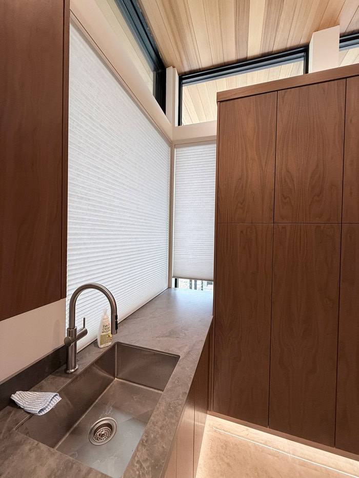 Bright kitchen featuring wooden cabinets, a stainless steel sink, and large windows with blinds in Clear Lake, Manitoba.