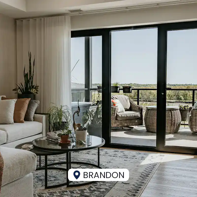 Bright living room with large glass doors opening to a balcony overlooking lush greenery, featuring comfortable seating, indoor plants, and stylish decor.