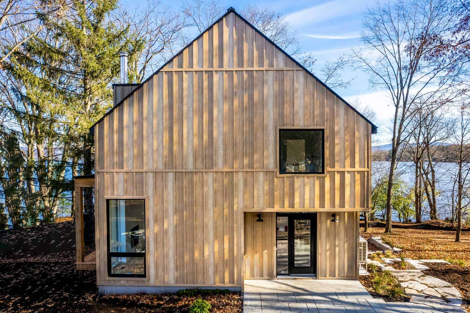 Modern wooden house under construction with large windows and natural surroundings.