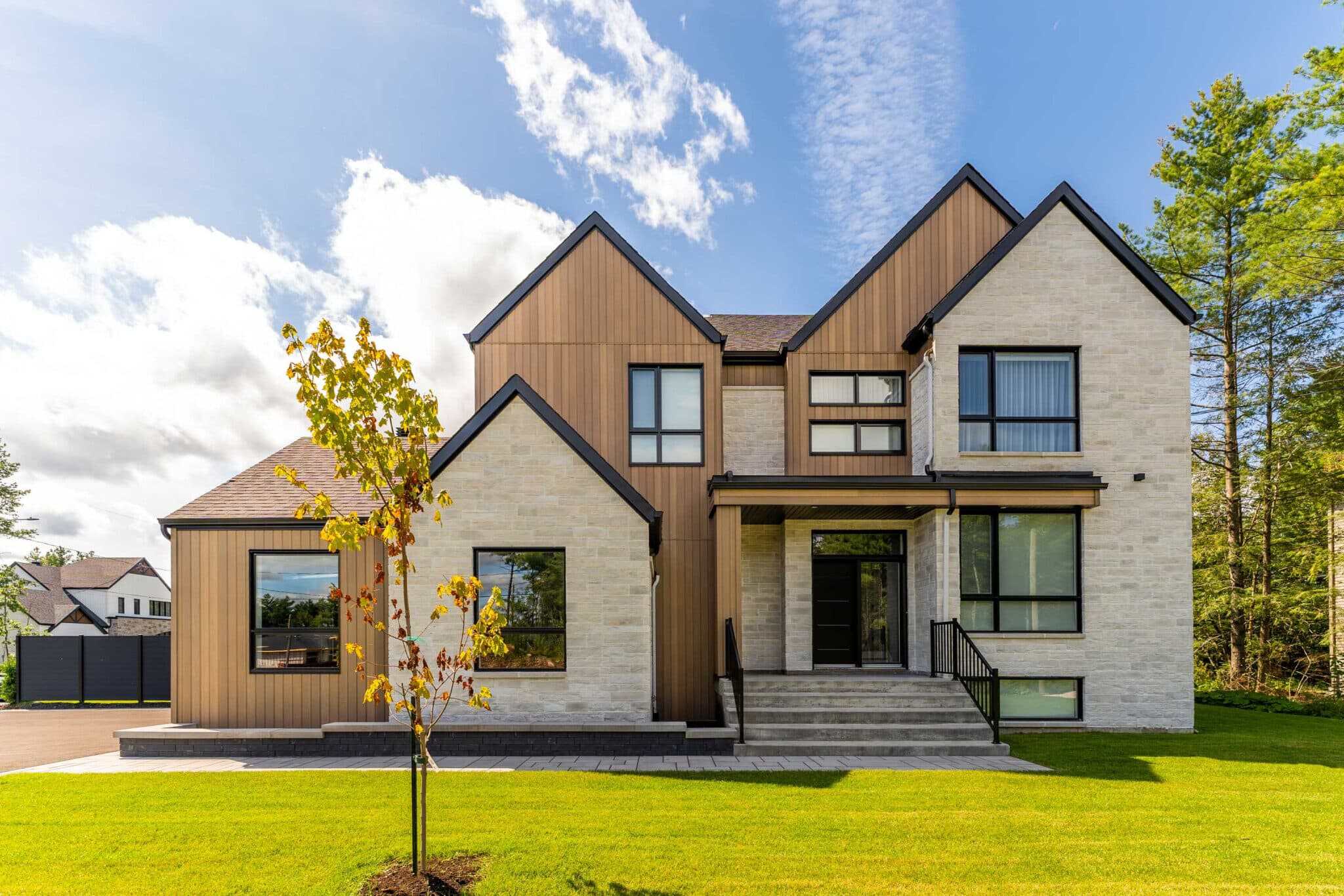 Modern house with mixed wood and stone exterior, large windows, and a landscaped front yard.