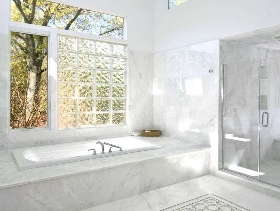 Elegant white marble bathroom with bathtub and glass shower enclosure, bright natural light, and sce.