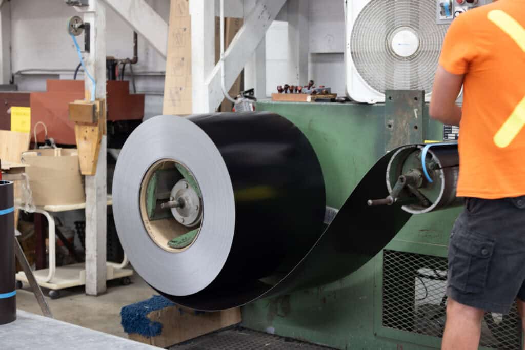Black metal coil being processed on industrial machinery at Tamar Building Products.