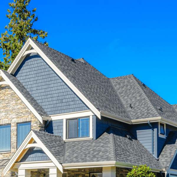 Slate roof shingles on a modern residential house with stone and blue siding, under a clear blue sky.
