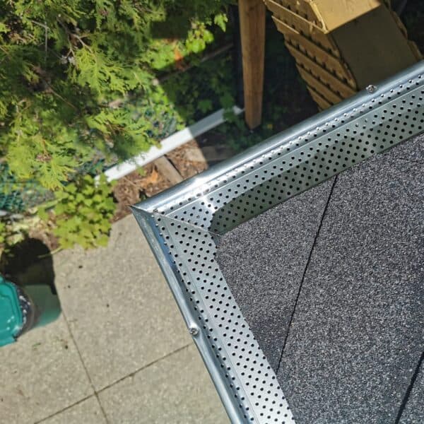 Metal gutter with perforated edge installed on a roof, surrounded by greenery and outdoor elements.