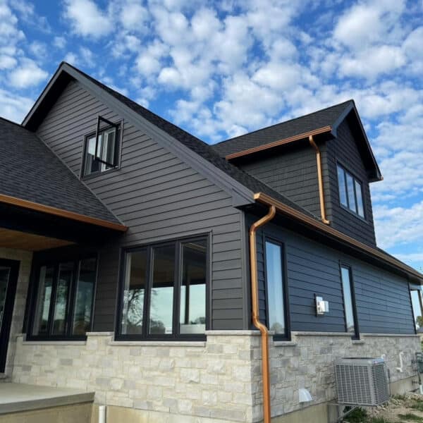 Black modern residential building with large windows and stone foundation, under a partly cloudy sky.