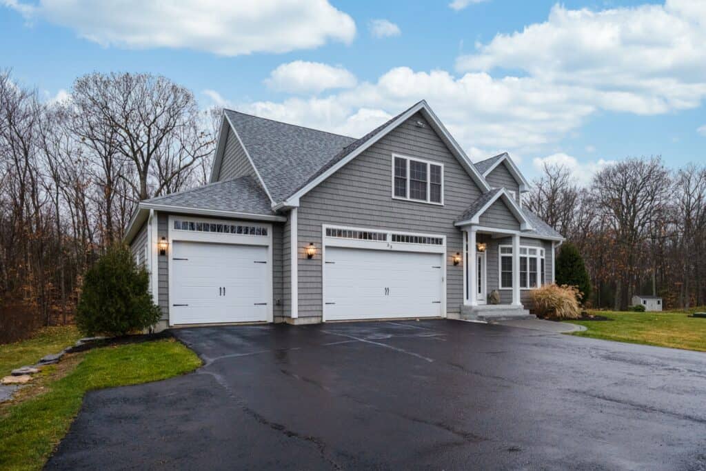 Newly constructed grey suburban house with a three-car garage and paved driveway.