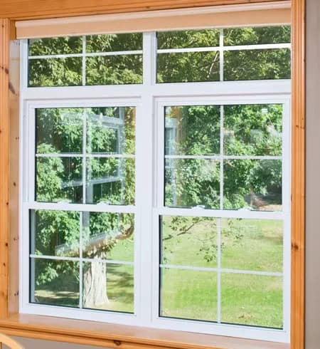 Vinyl window with multiple panes installed in a wooden frame, offering a clear view of lush green tr.