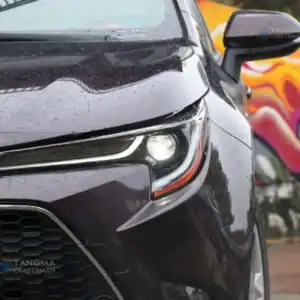 Close-up of a black car's front with rain droplets, highlighting auto parts and design.