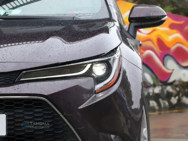 Close-up of a black car's front with rain droplets, highlighting auto parts and design.