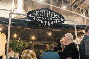 Hand painted Brothers Beer sign at Taranaki Beer Festival with patrons enjoying craft beers under festival tent.
