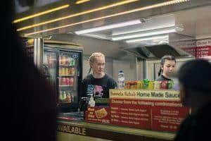 Candid shot of two women working at a food stand during Taranaki Beer Festival, serving kebabs and drinks at the event.