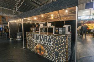 Brightly lit Tuarara Brewing Co. beer stall at the Taranaki Beer Festival, showcasing craft beers in a lively festival setting.