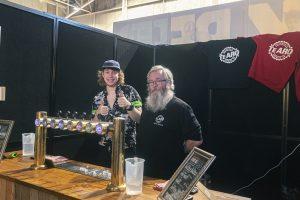 Bright young man and bearded man smiling at Taranaki Beer Festival, serving craft beers at Tearo Brewing Co. booth.