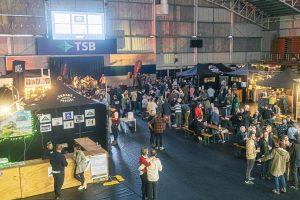 Vibrant scene at Taranaki Beer Festival with craft beers, live music, and lively crowd in an indoor venue in New Zealand.