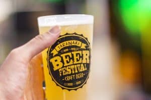 Cerveja artesanal no Festival de Cerveja de Taranaki, Nova Zelândia, com logo destacado na taça de vidro.