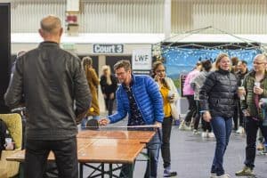 Colorful crowd enjoying Taranaki Beer Festival at indoor venue; people socialising, playing table tennis, and tasting craft beers.