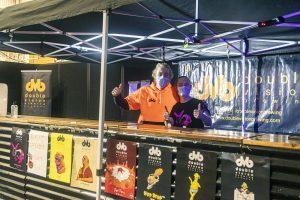 Brightly colored beer festival stall at Taranaki Beer Festival with staff wearing masks and giving thumbs up.