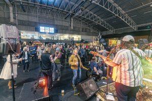 Vibrant crowd enjoying live music at the Taranaki Beer Festival in a spacious indoor venue.