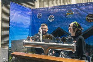 Creative NZ craft beer festival stand with smiling staff, showcasing diverse tap beers, at Taranaki Beer Festival.