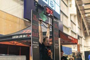 Man hanging from bar at Taranaki Beer Festival, lively craft beer event in New Zealand, fun bar competition, beer festival entertainment.