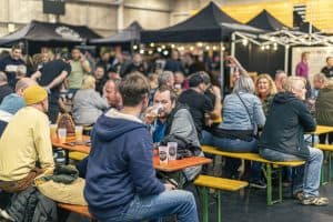 Vibrant scene at Taranaki Beer Festival with people enjoying craft beers and live music in an outdoor setting.
