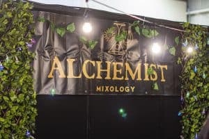 Vibrant Alchemist Mixology stand at Taranaki Beer Festival with greenery and decorative lighting.