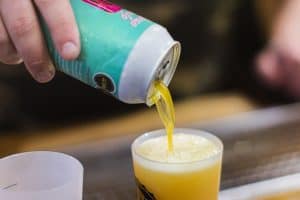 Brightly coloured canned craft beer being poured into a plastic cup at Taranaki Beer Festival.