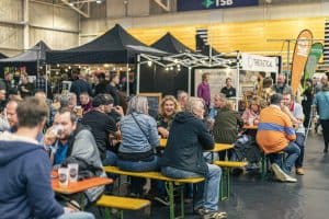 Vibrant scene at the Taranaki Beer Festival with people enjoying craft beers and food under tents Indoor event atmosphere in Taranaki.