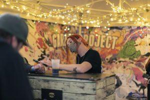 Festival beer tasting at Taranaki Beer Festival with vibrant street art background and fairy lights.