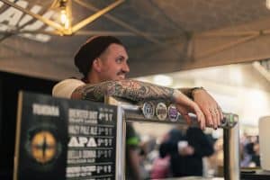 Vibrant male bartender with colorful tattoos serving beer at Taranaki Beer Festival in New Zealand.