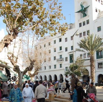 Imagen de la plaza principal en Tetuán con árboles, personas y edificios emblemáticos.