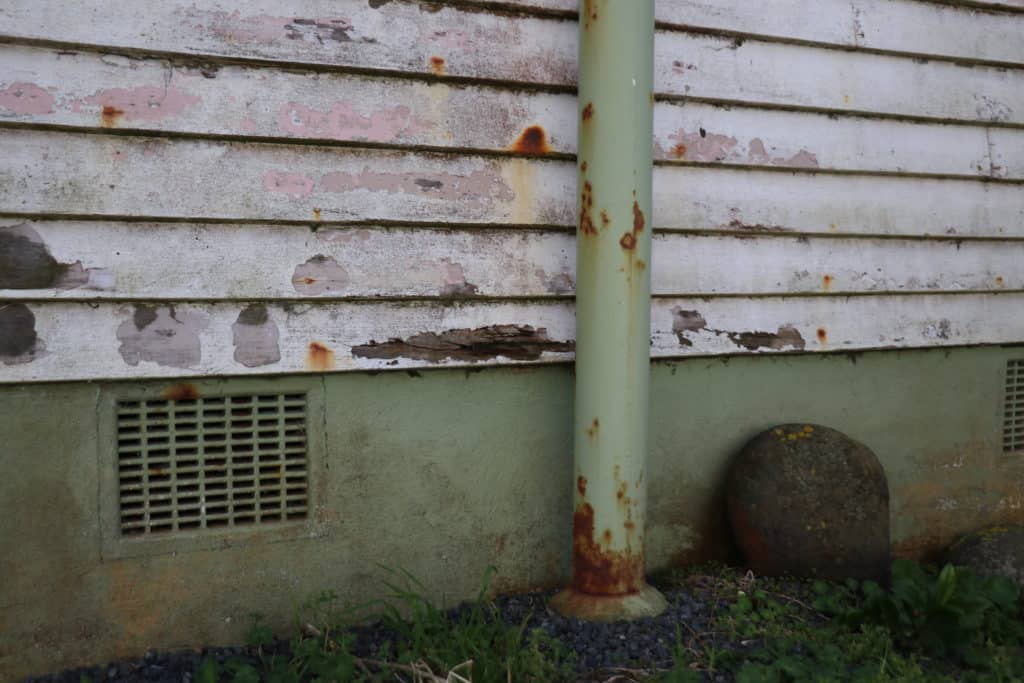Old weathered wooden house siding with rusted pipe and vents, showcasing neglected building maintenance.