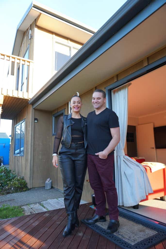 Modern Te Tumu Kāinga house exterior with happy couple standing on the porch.