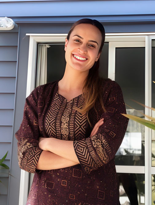 Bright young woman smiling outside a modern home, representing Te Tumu Kāinga housing solutions.
