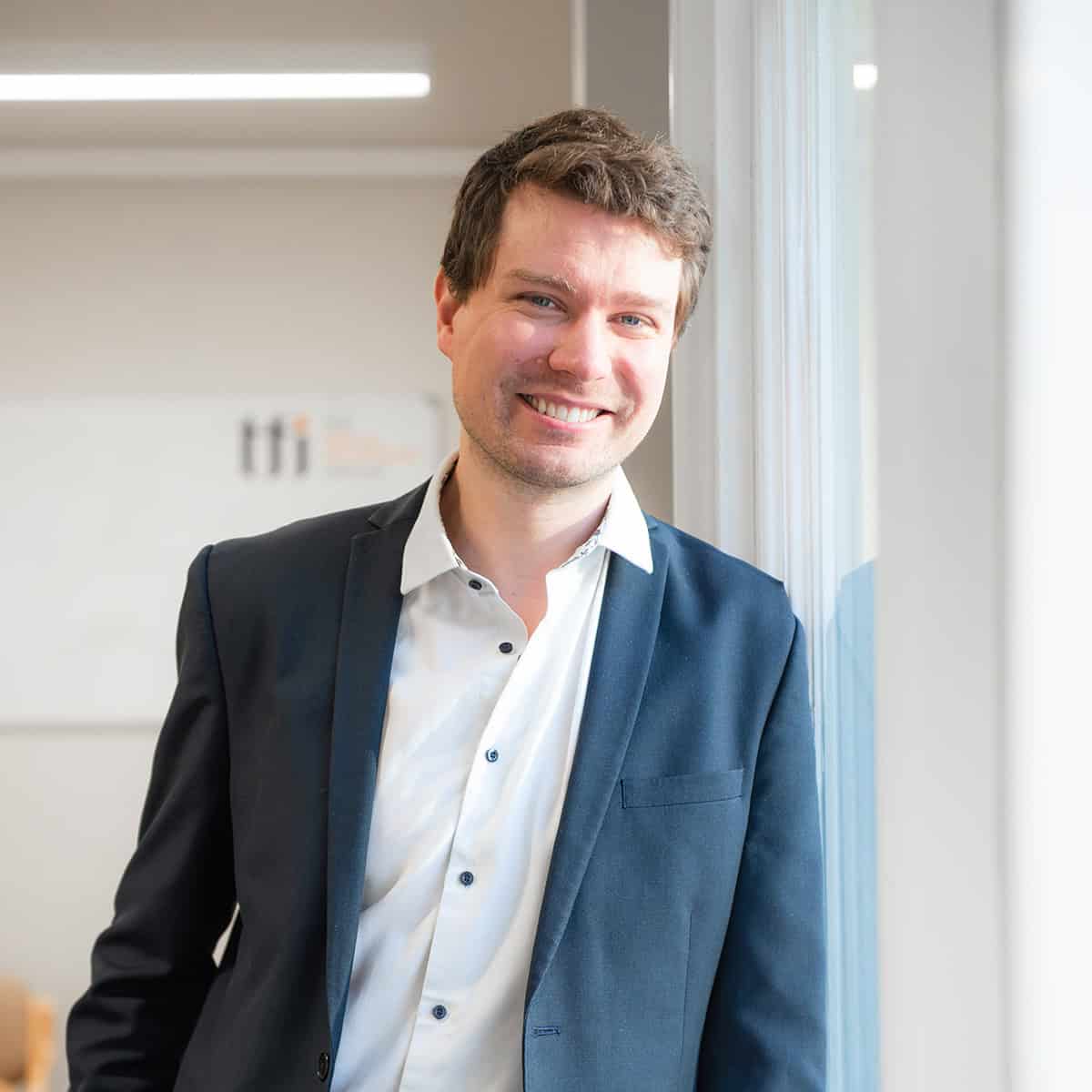 Smart businessman smiling in modern office environment, professional corporate interior, representing TFI Group UK.