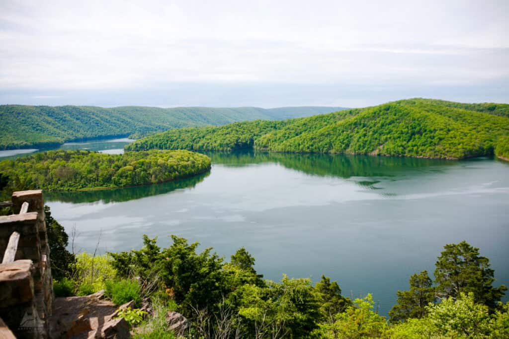 Hawn’s Overlook provides a stunning panoramic view of Raystown Lake, surrounded by rolling green mountains. The still water reflects the bright sky, and the overlook is framed by lush trees and a rocky ledge, creating a breathtaking natural scene.
