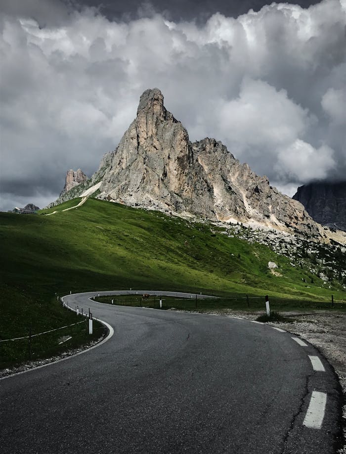 Curved road leading to majestic mountains beneath a dramatic cloudy sky.