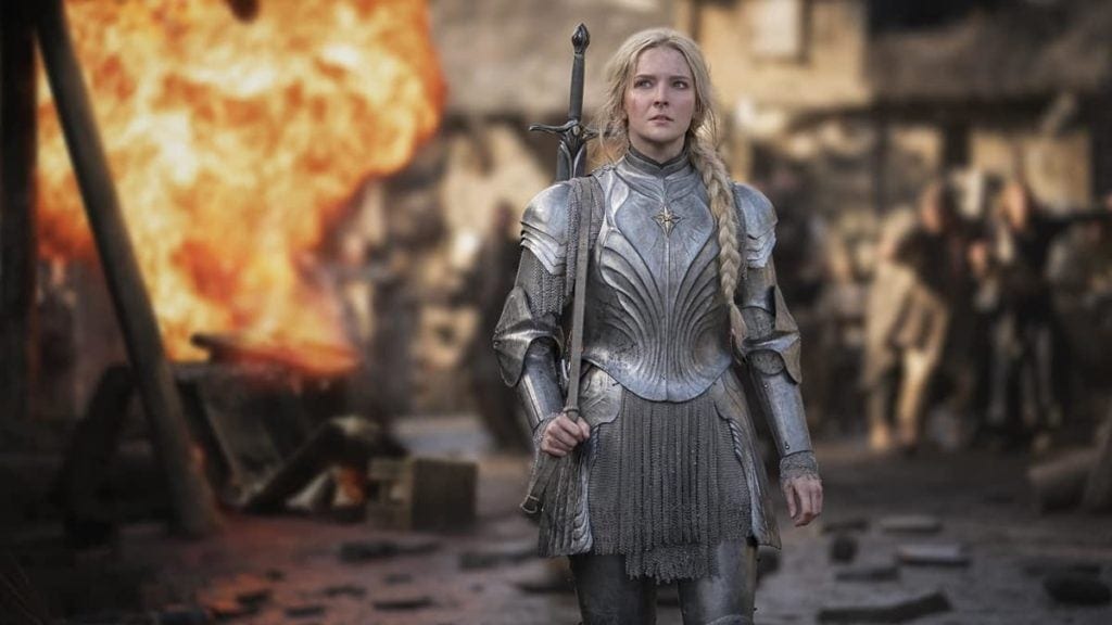 Seasons 3-5 of The Lord of the Rings: The Rings of Power- Galadriel walking in her silver armor with a large burst of fire and people in the background. 