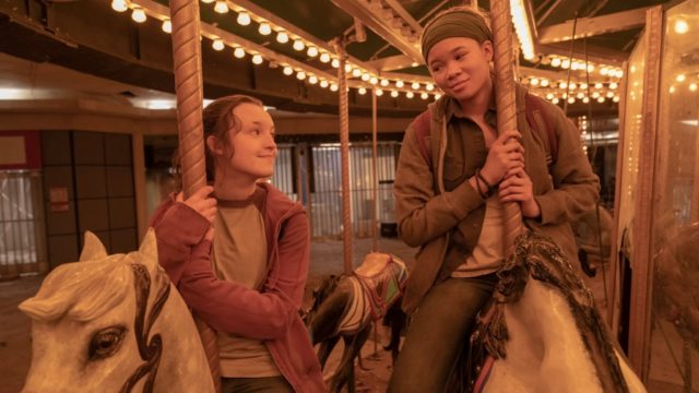 A carousel with two young girls sitting on painted horses at an amusement park.
