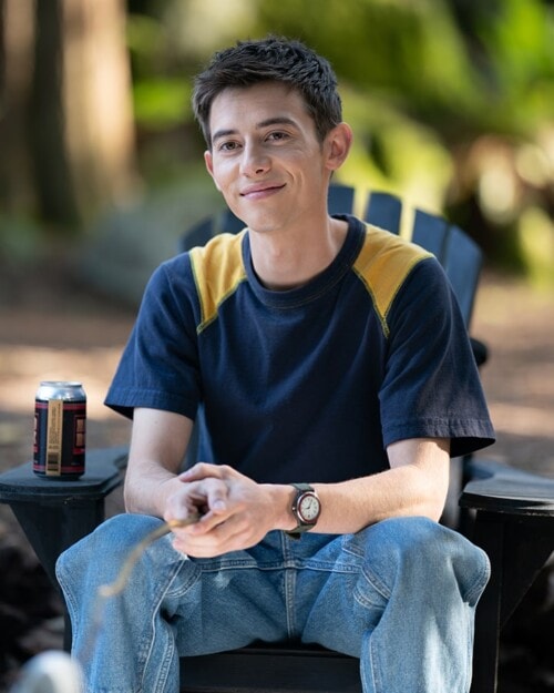 Young man sitting outdoors with a soda can, smiling, in a casual setting.