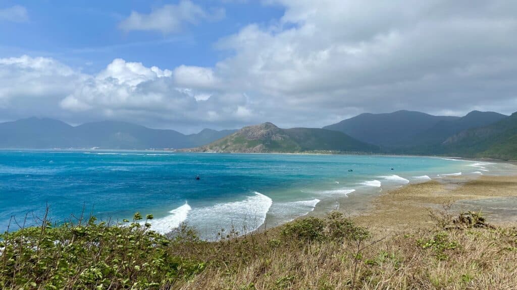 Bãi Đất Dốc ở Côn Đảo. Sóng trắng đầu lớp lớp. Bãi cát vàng hoang sơ. Xa xa là núi.