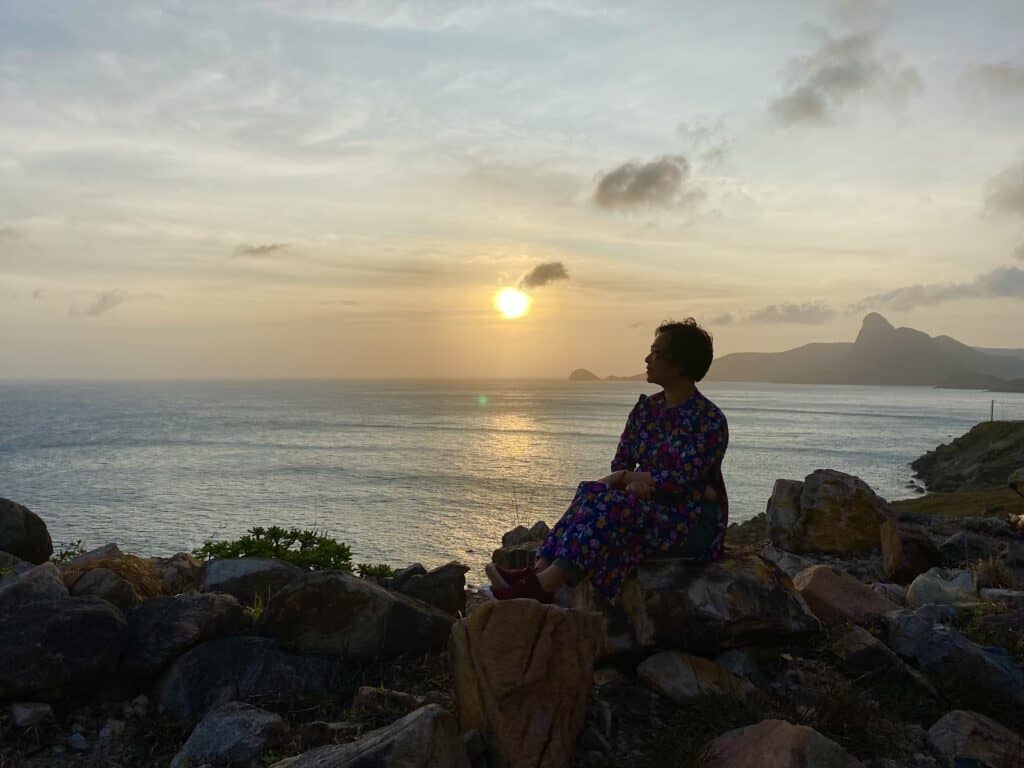 Mũi Cá Mập, Côn Đảo. Mặt trời lặn xuống biển. Xa xa là dãy núi. Một người ngồi ngắm hoàng hôn.