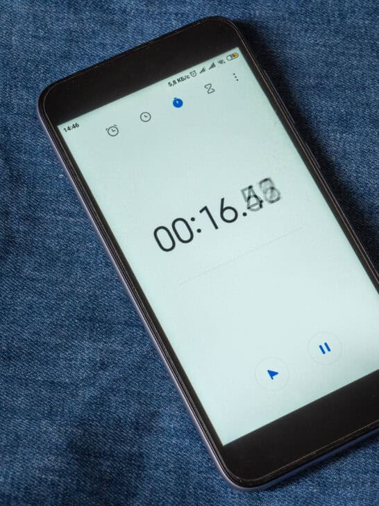 Running time on the screen of the device. Black smartphone with open Stopwatch app. Endless running time concept. Against the blue jeans.