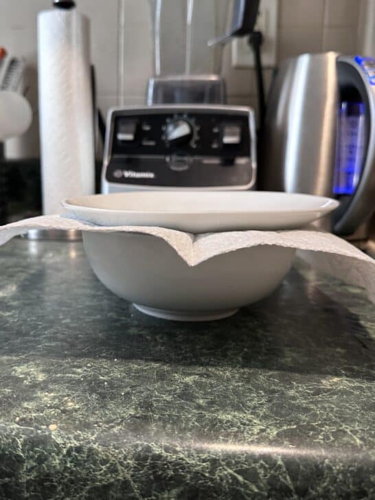 picture of a salad bowl topped with a paper towel topped with a plate to seal it to store royal icing
