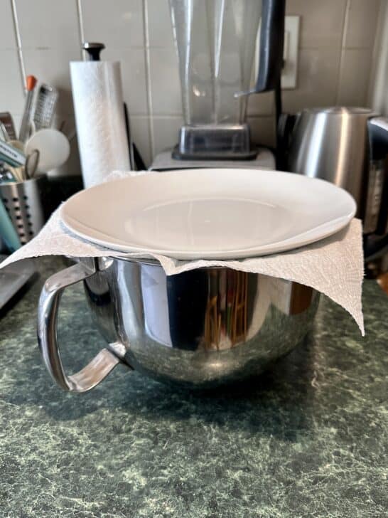 photo of mixing bowl topped with a paper towel and topped with a plate to seal it for storing royal icing